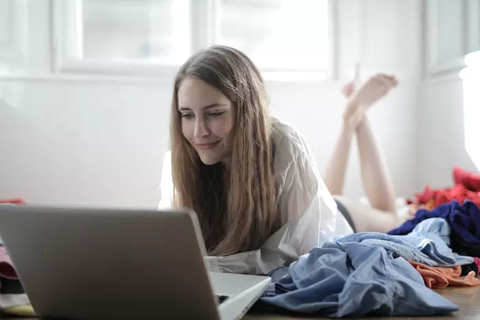 En kvinna ligger på sängen och tittar på datorn